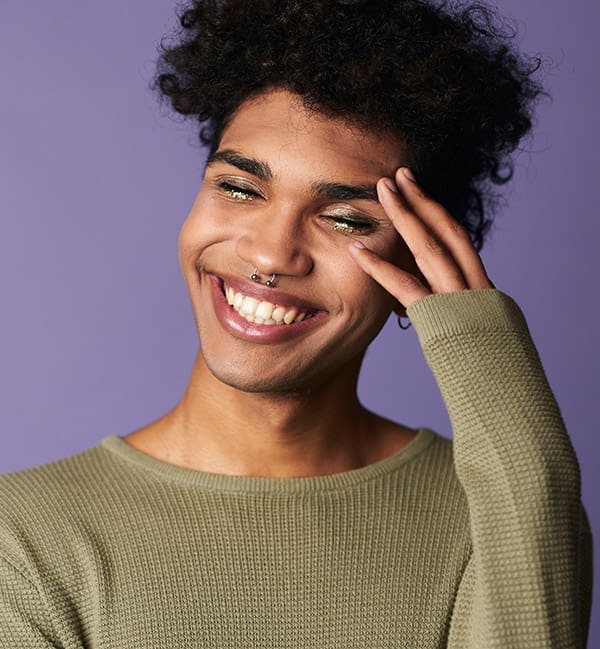 Close-up smiling african american male with afro hairstyle. Portrait of handsome transgender young man. Happy casual dressed trans gender model on purple background. Fashion